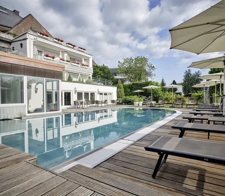 Outdoorpool mit Blick auf die weiße Fassade des Hotel Reppert mit schwarzen Liegen