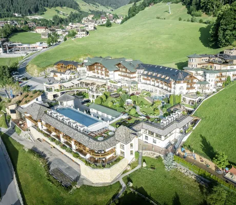 Luftaufnahme der Hotelanlage des STOCK resort mit mehreren Gebäuden, Außenpool und umliegenden grünen Wiesen und Wäldern
