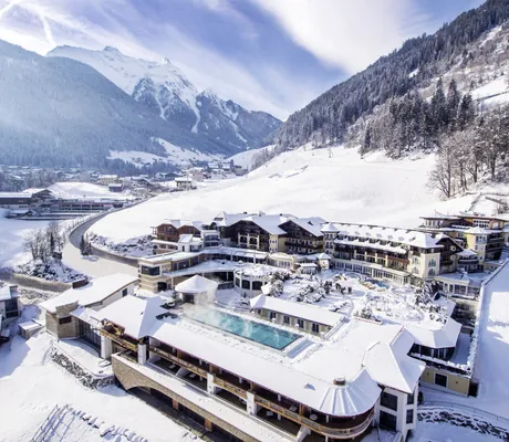 Blick auf die Hotelanlage des STOCK resort im Winter mit Outdoorpool, umgeben von verschneiter Berglandschaft