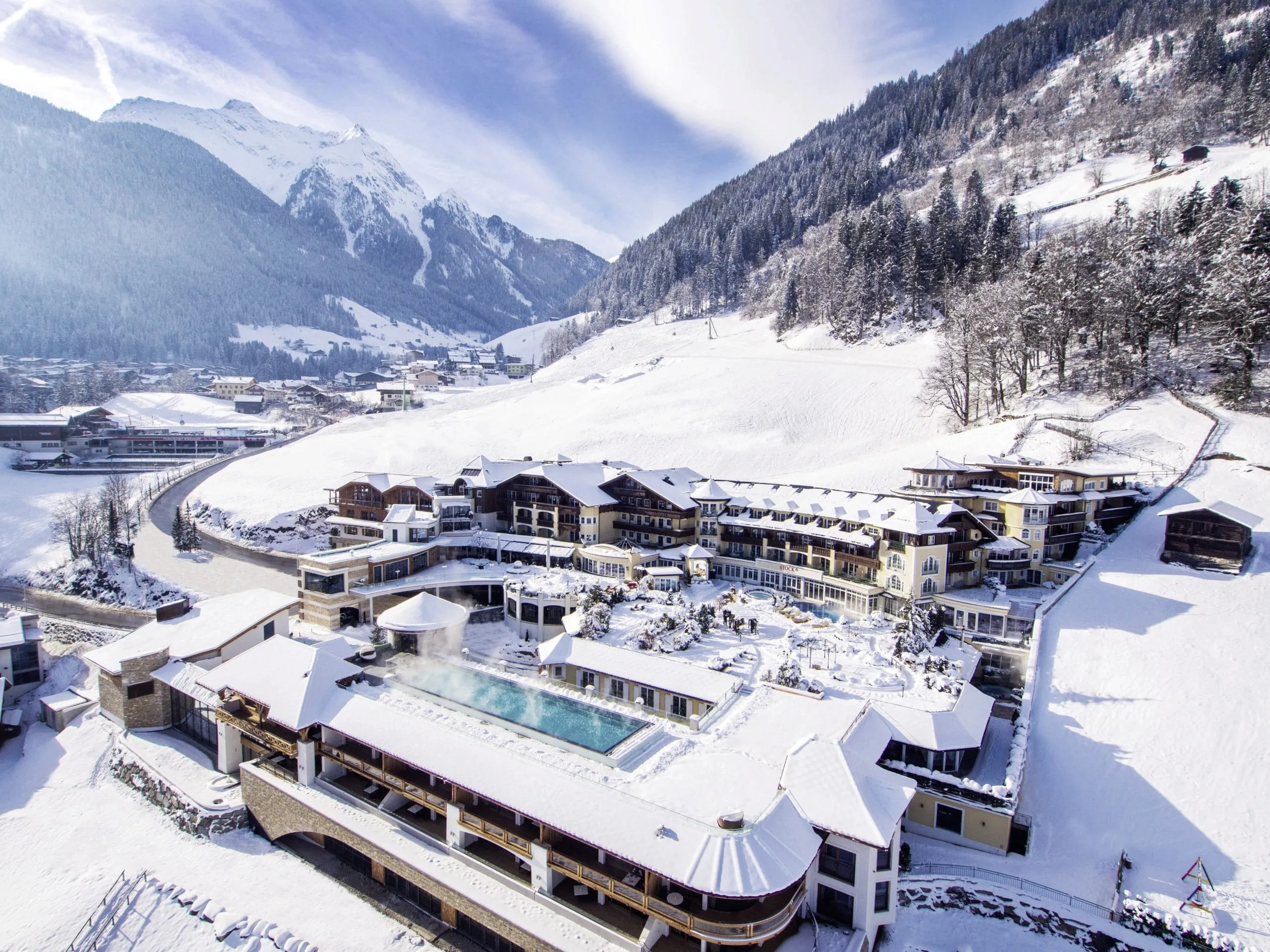 Blick auf die Hotelanlage des STOCK resort im Winter mit Outdoorpool, umgeben von verschneiter Berglandschaft
