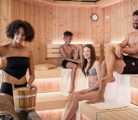 Familie in Badebekleidung in einer Sauna des STOCK resort, Frau macht einen Aufguss