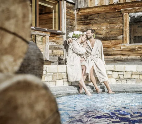 Zwei Personen in beigefarbenen Bademänteln entspannen am Rand des Outdoor-Whirlpools des STOCK resort