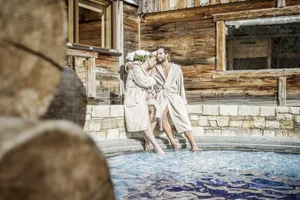 Zwei Personen in beigefarbenen Bademänteln entspannen am Rand des Outdoor-Whirlpools des STOCK resort