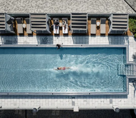Luftaufnahme des Outdoorpools im STOCK resort mit schwimmender Person, Liegen und Himmelbetten am Beckenrand