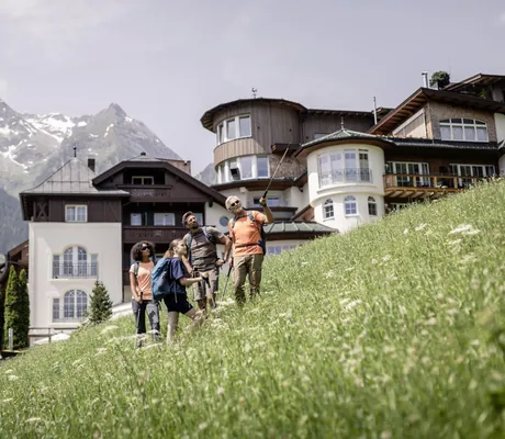 Vier Personen in Wanderkleidung auf einer Wiese vor dem STOCK resort mit Bergen im Hintergrund