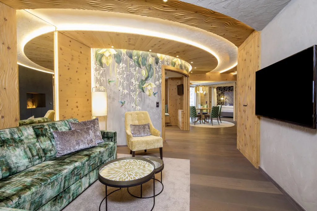 Suite im STOCK resort mit grün, gemustertem Sofa, gelbem Sessel vor Tapete, runden Tischen mit Muster, Holzverkleidung und beleuchtetem, runden Deckenelement