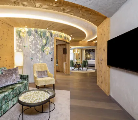 Suite im STOCK resort mit grün, gemustertem Sofa, gelbem Sessel vor Tapete, runden Tischen mit Muster, Holzverkleidung und beleuchtetem, runden Deckenelement