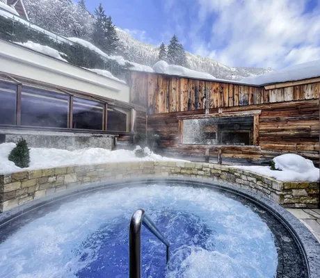 Outdoor-Whirlpool im STOCK resort, umgeben von Steinmauer im Winter mit Schnee auf Dächern