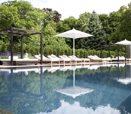 Outdoorpool im Schloss Fleesensee mit weißen Sonnenschirmen und weißen Ruheliegen am Beckenrand