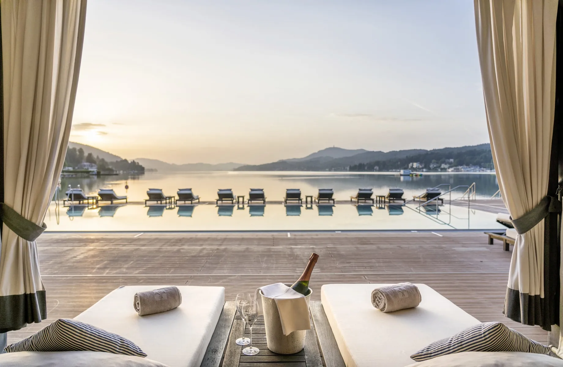 Blick von der Ruheliege mit Champagnerkühler aus direkt auf den Wörthersee und die Ruheliegen am Pool