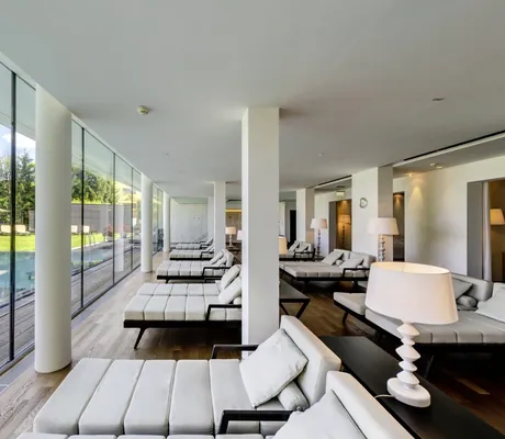 Ruheraum im Schlosshotel Velden mit weißen Liegeflächen und weißer Stehlampe mit Blick auf Outdoorpool