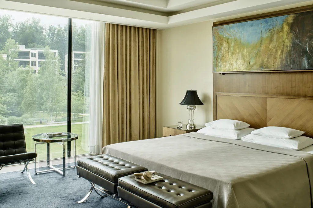 Doppelzimmer im Schlosshotel Velden mit Gemäde über dem Bett und zwei Lederhockern vor dem Bett