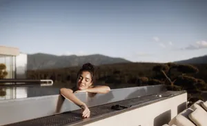 dunkelhaarige Frau mit Dutt liegt mit geschlossenen Augen am Rand des Skypools des Hotel Solvie