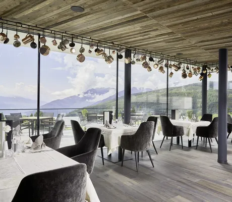 gedeckte Tische im Restaurant vor dem Panoramafenster mit Töpfen an der Decke im Sonnenberg Panorama Dolomites Wellbeing