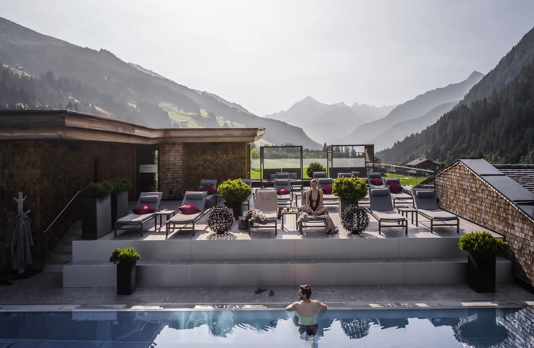 Mann steht am Beckenrand des Skypools im Tuxerhof und Frau sitzt auf einer Liege am Rand