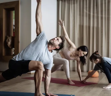 Paar macht im großes Zimmer im Tuxerhof Yoga und wird von Yogalehrerin angeleitet