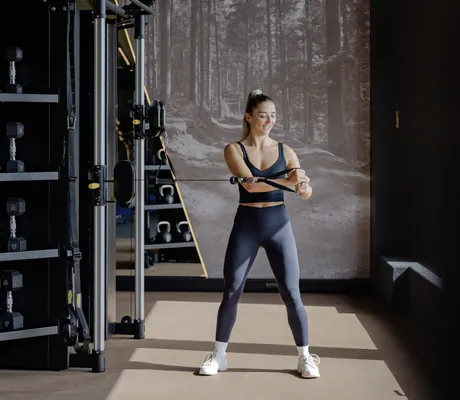 Frau in schwarzem Gym-Outfit zieht an der Kinesiswand an einem Gewicht