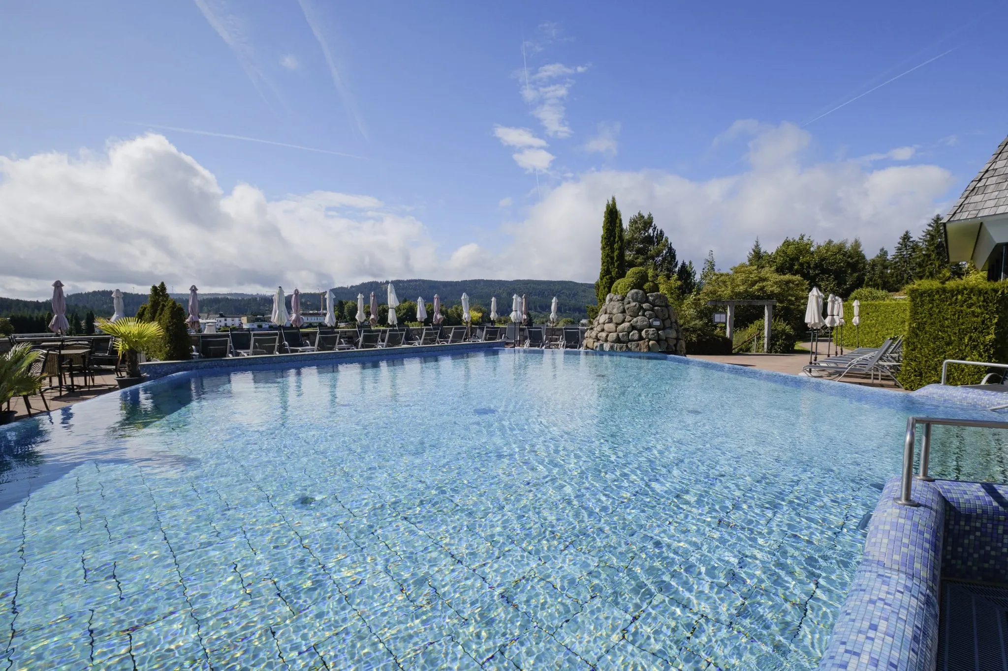 Outdoorpool im Vier Jahreszeiten am Schluchsee mit Felshaufen und weißen Sonnenschirmen
