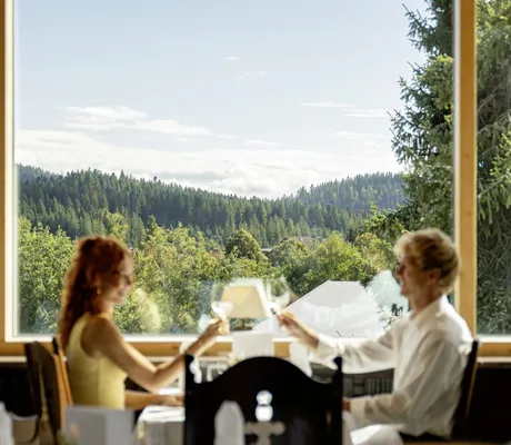 Paar prostet sich im Restaurant des Vier Jahreszeiten am Schluchsee zu vor der Baumkulisse des Schwarzwalds