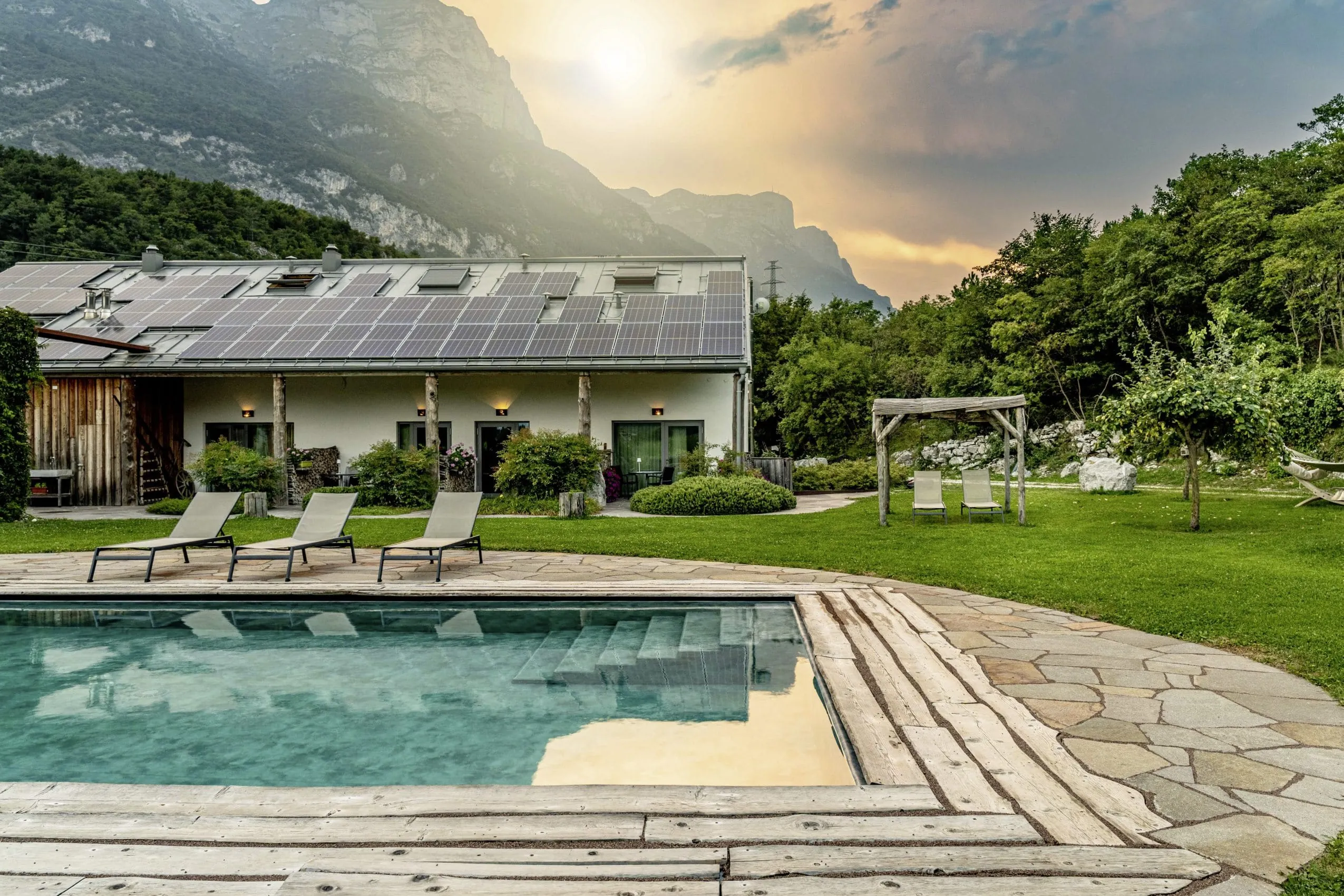 Bioschwimmbad des Adulty only-Refugium Agritur La Dolce Mela mit Liegest&uuml;hlen und Bergpanorama in der Abendd&auml;mmerung