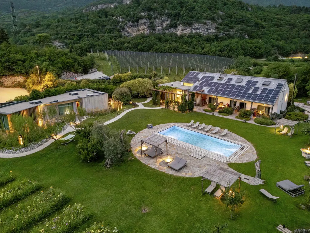 Luftaufnahme des Agritur La Dolce Mela mit Bioschwimmbad, Garten und Apfelplantagen vor Bergkulisse