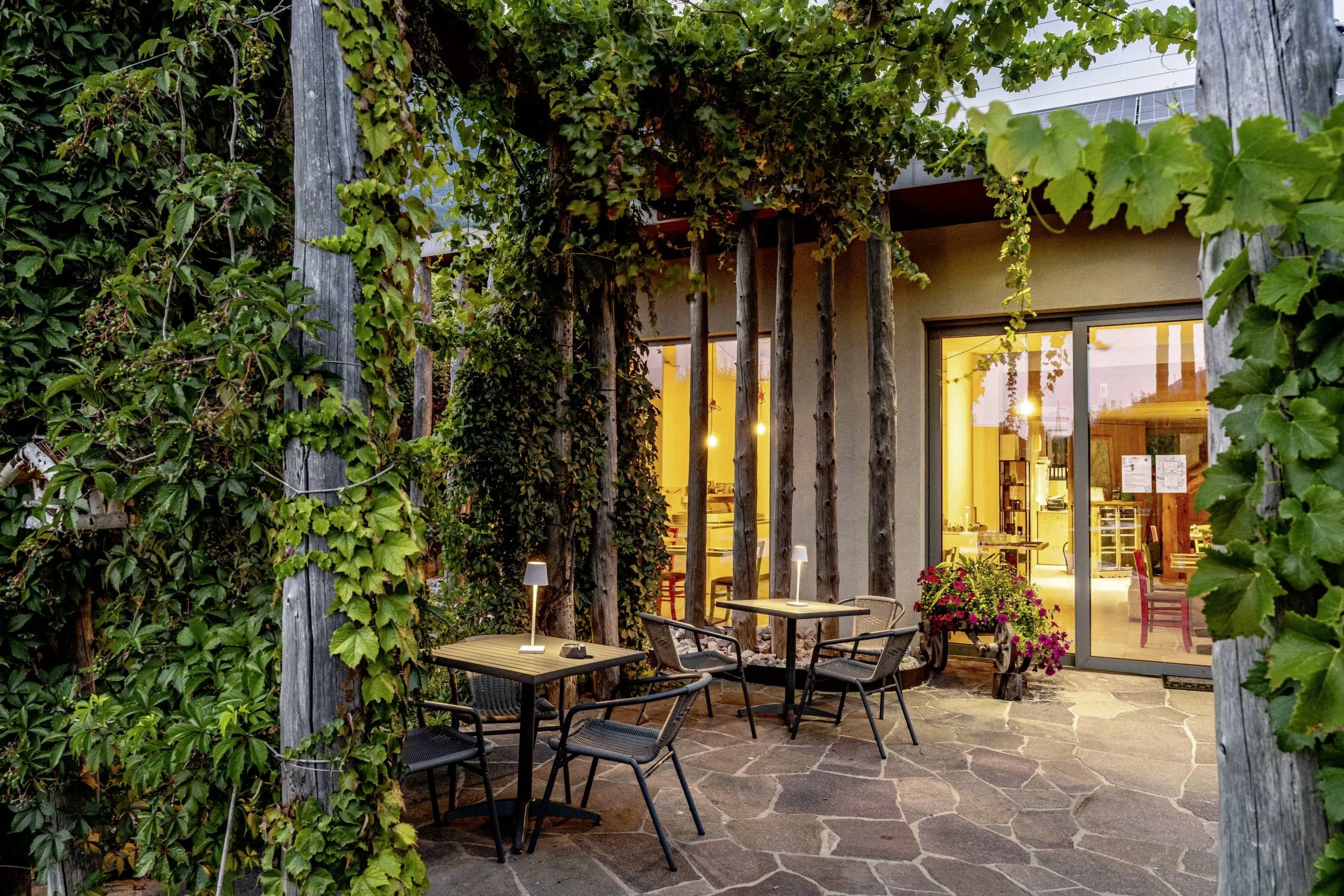 Begr&uuml;nte Veranda mit Sitzbereich und Blick in den beleuchteten Innenraum der Agritur La Dolce Mela