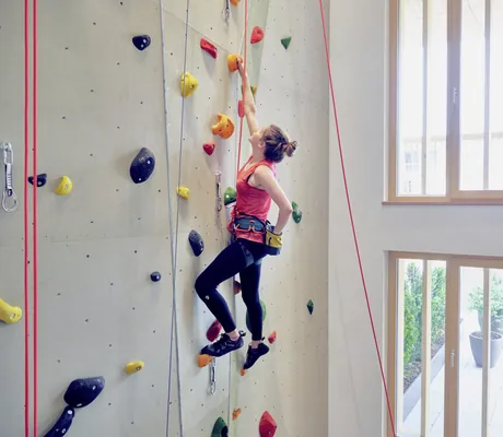 Frau mit rotem Shirt klettert angeseilt an der Kletterwand des Falkensteiner Kronplatz