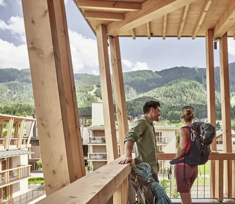 Paar steht mit Rucksäcken und Wanderausrüstung auf dem Balkon des Falkensteiner Kronplatz