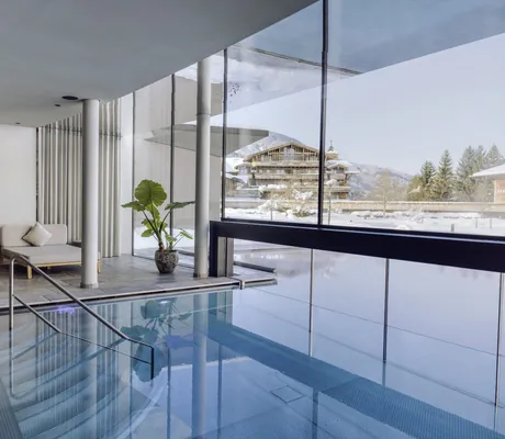 Moderner Indoorpool des Naturresort PURADIES mit Glasfront, Blick auf Winterlandschaft, Sitzbereich mit gemütlichen Daybeds
