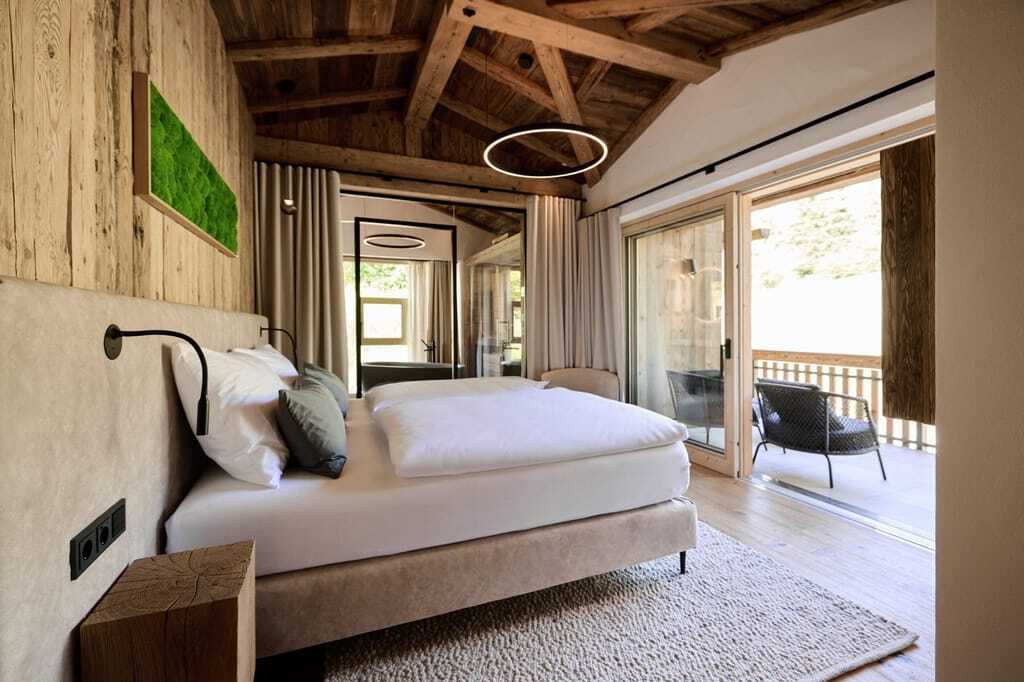 Modernes Schlafzimmer in einem der Ziegelberg Chalets mit großem Bett, Holzbalkendecke, bodentiefen Fenstern und Balkon mit Stühlen