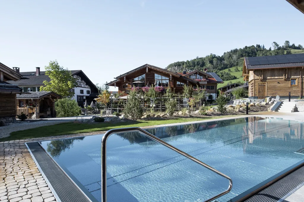 Au&szlig;enpool umgeben von den Alpzitt-Chalets und bewaldeter H&uuml;gel im Hintergrund