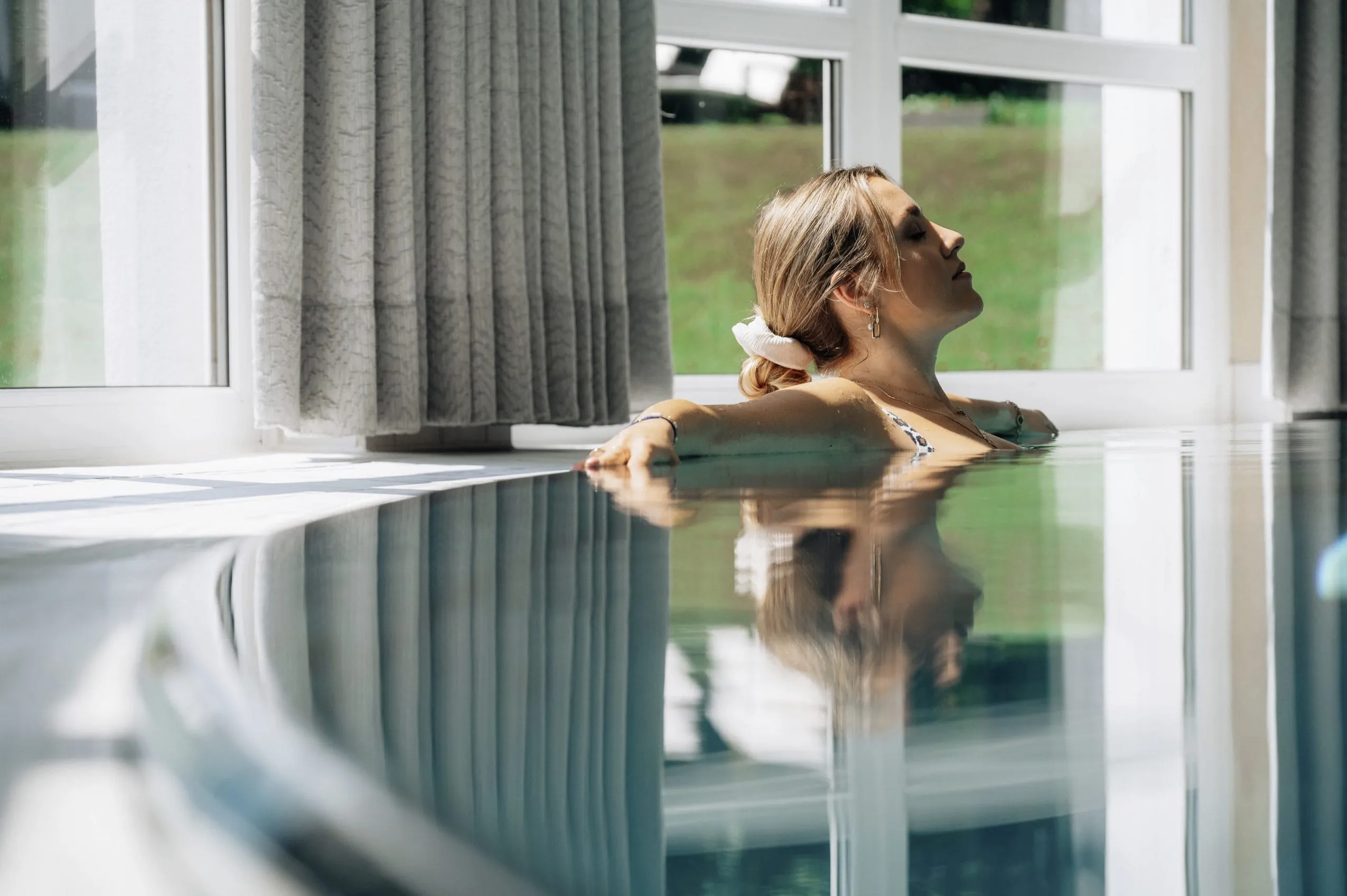 Junge Frau entspannt am Rande des Indoorpools im Wellnesshotel Der Sonnenhof