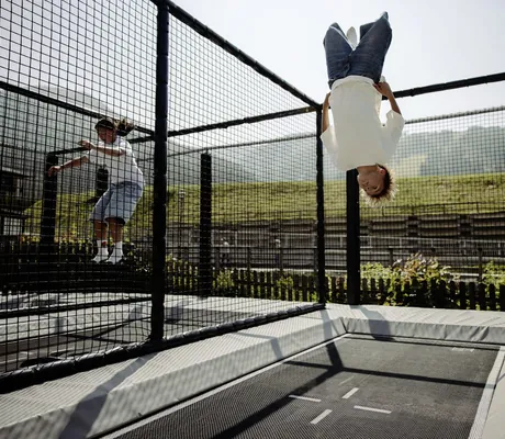 Zwei Kinder springen auf einem rechteckigen Trampolin mit Netzumrandung im Resl Resort