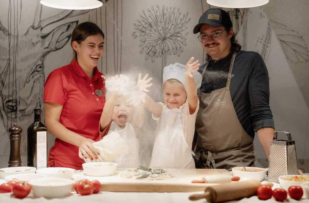 zwei Kinder in Kochoutfit backen mit ihren Eltern im Alpin SPA Hotel Tuxerhof Pizza