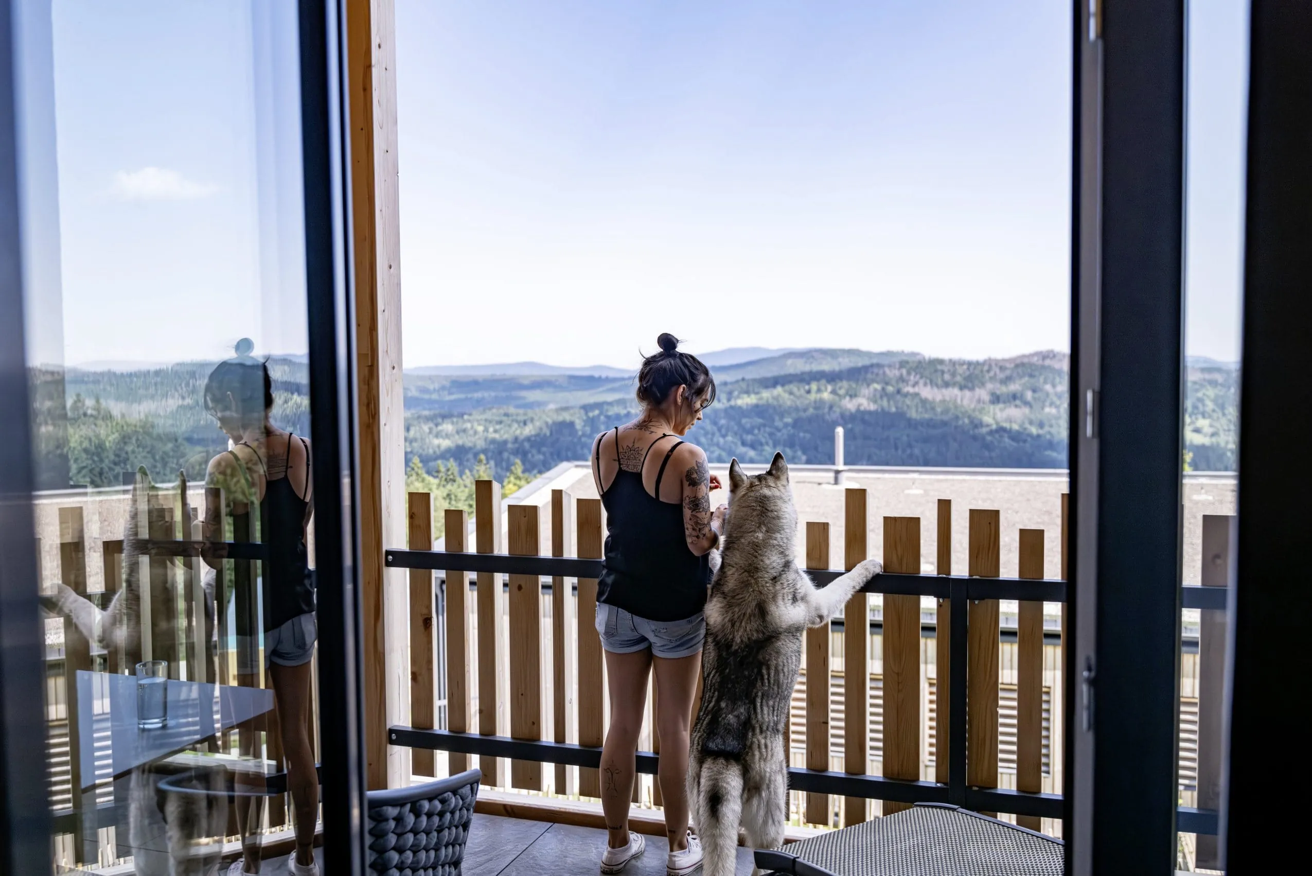 Frau steht mit Hund am Balkon des Lofts im Hunderesort Waldeck und schaut in die Ferne