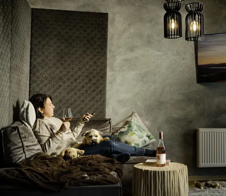 Frau liegt mit Hund auf dem Schoß auf dem Sofa im Hunderesort Waldeck und trinkt ein Glas Wein