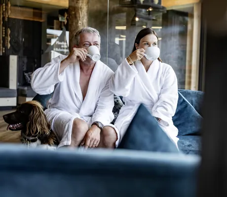 Paar im Bademantel trinkt im Spa des Hunderesort Waldeck Kaffee und Hund liegt daneben