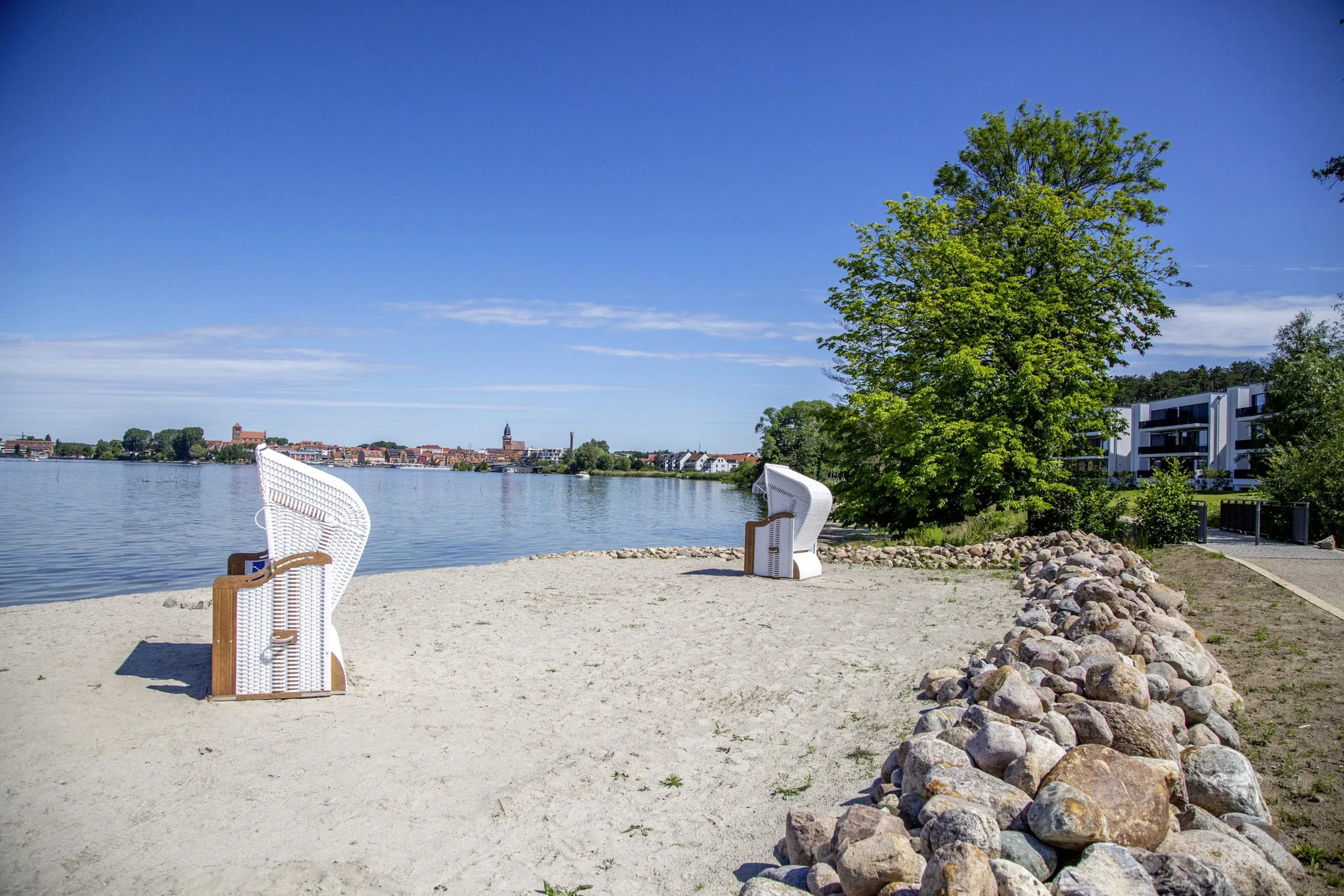 Wei&szlig;er Strandkorb am Sandstrand mit Blick auf die M&uuml;ritz und die Stadt Waren