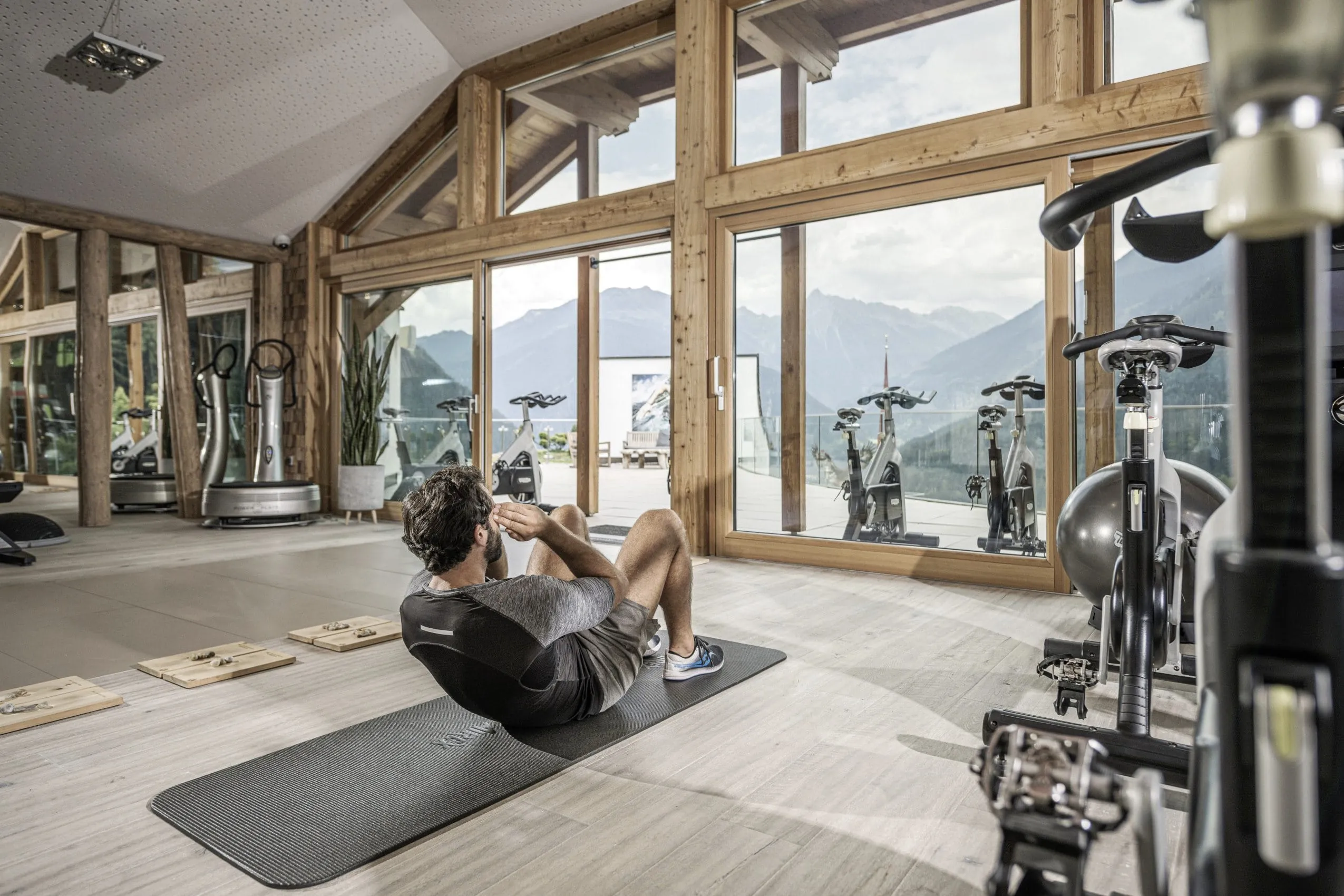 Mann macht Sit-ups auf Sportmatte in hellem Fitnessraum des STOCK resort mit gro&szlig;en Fenstern und Bergblick