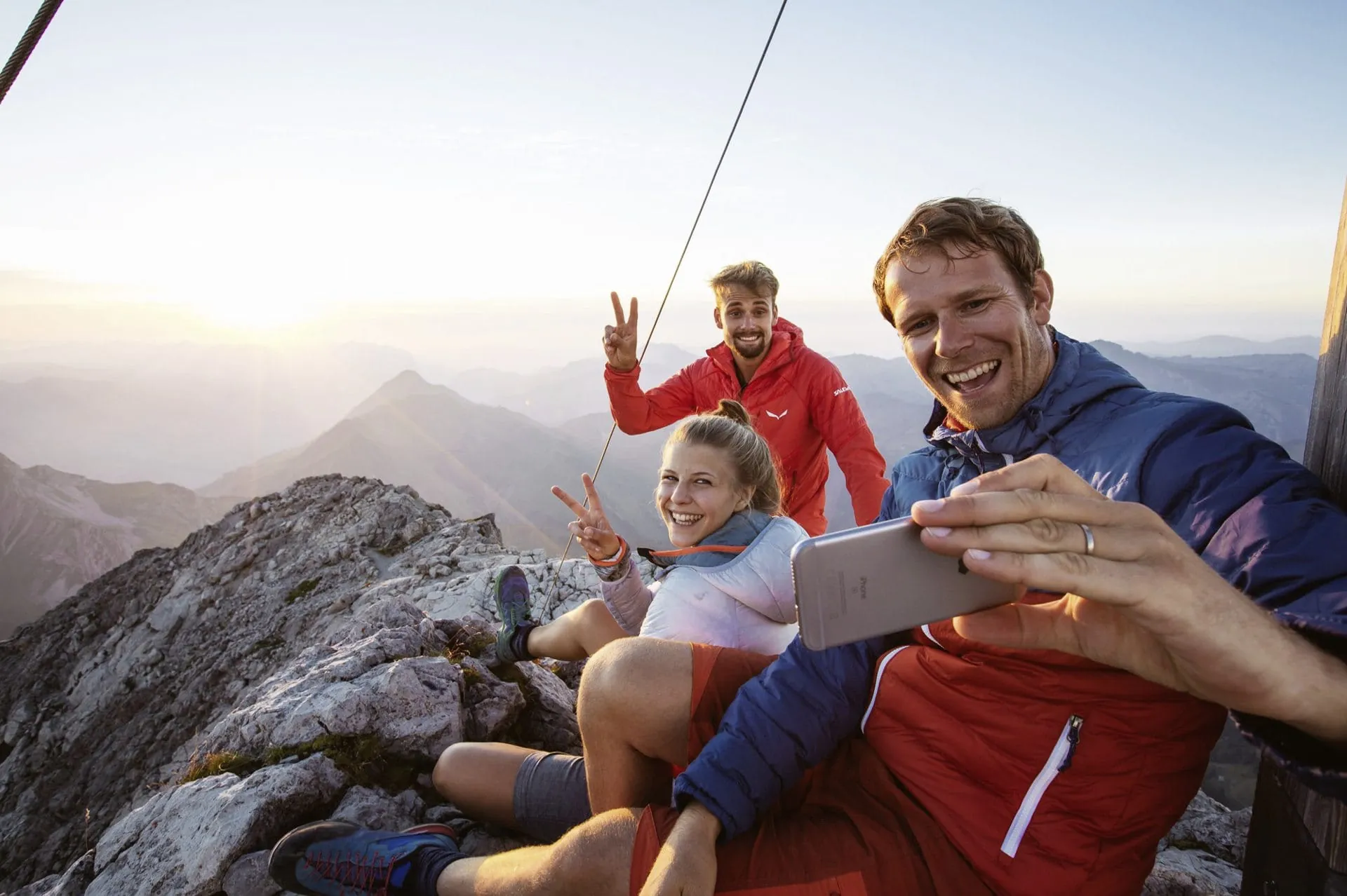 Drei Wanderer machen Selfie auf Berggipfel in Wanderregion Warth-Schr&ouml;cken bei Sonnenuntergang
