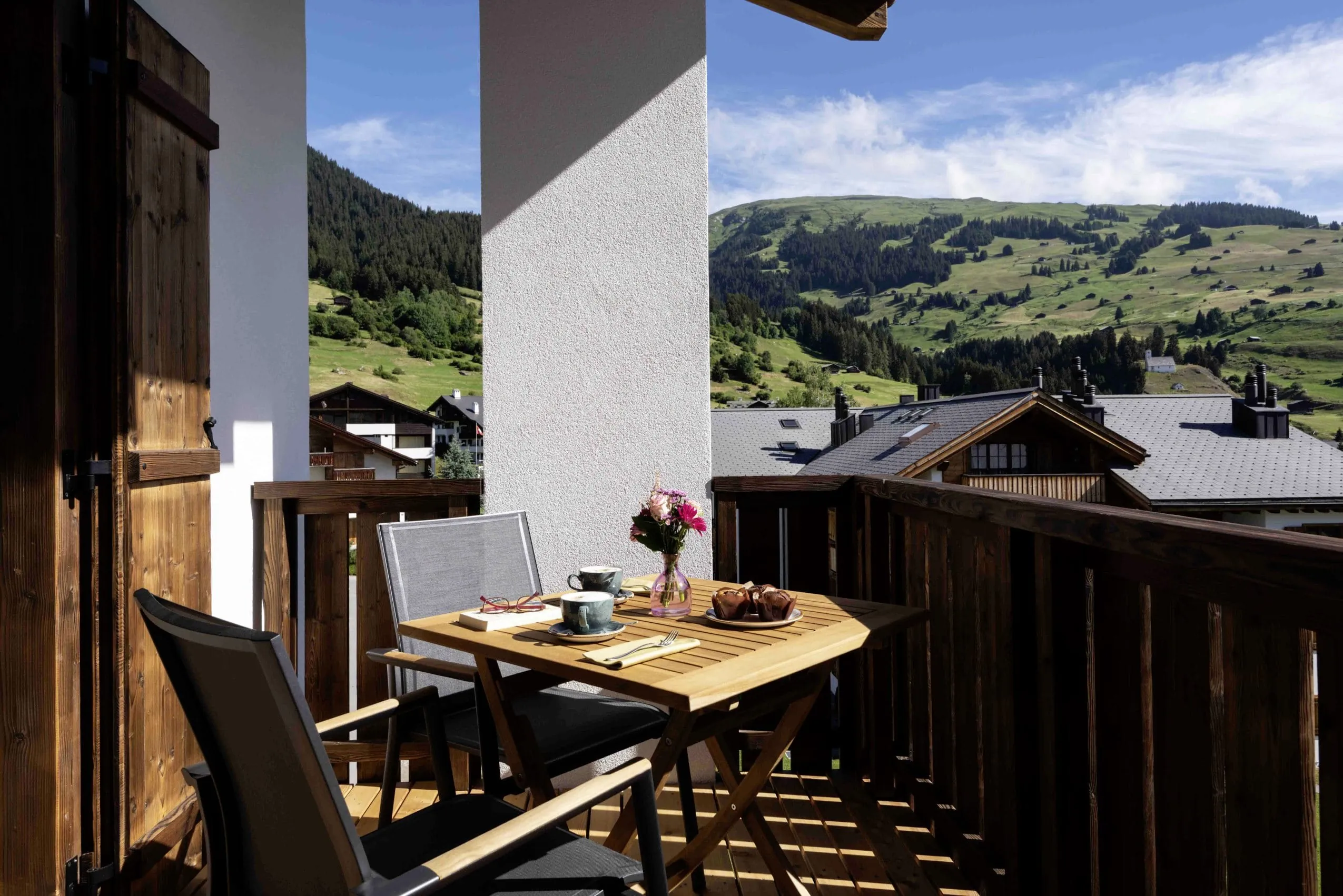 Balkon mit gedecktem Tisch und Panoramablick auf gr&uuml;ne Berglandschaft in Brigels
