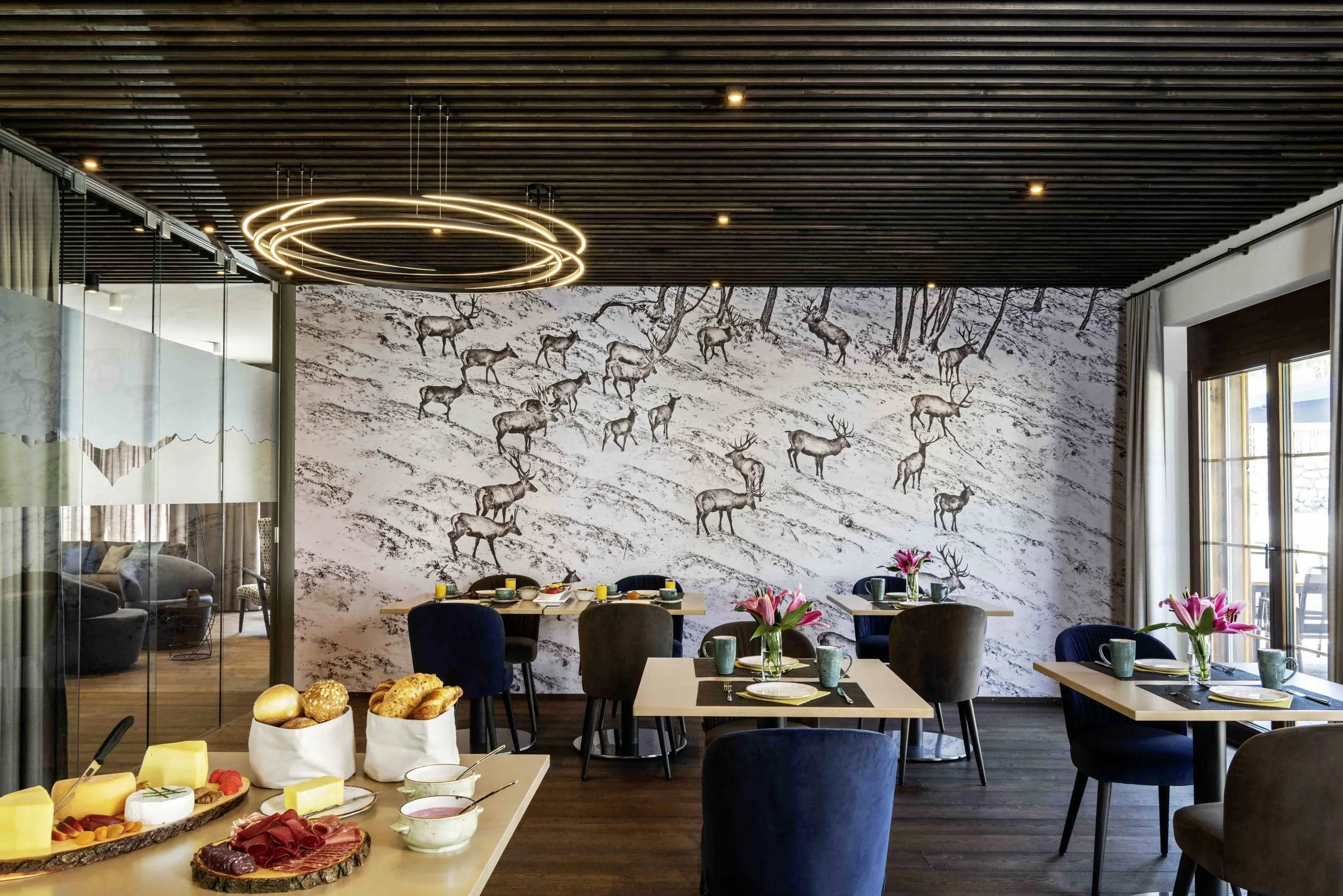Fr&uuml;hst&uuml;cksraum im Wanderhotel Mischun mit Hirsch-Fototapete, gedeckten Tischen und Ring-Deckenleuchte