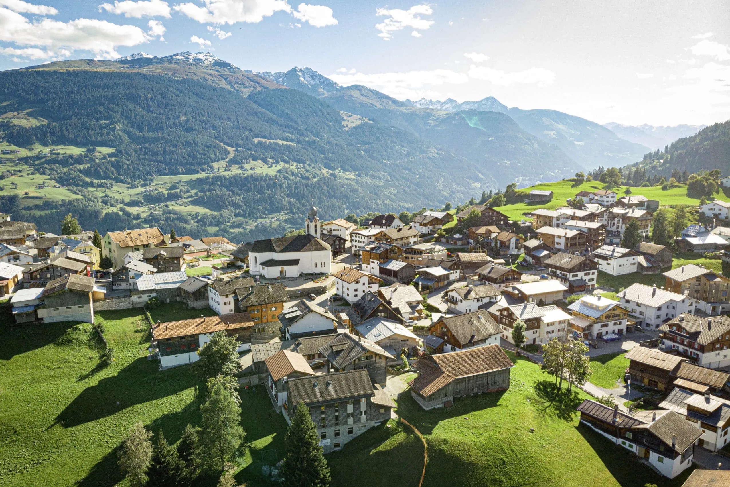 Luftaufnahme des Bergdorfs Brigels im Sommer mit traditionellen H&auml;usern und Alpenpanorama