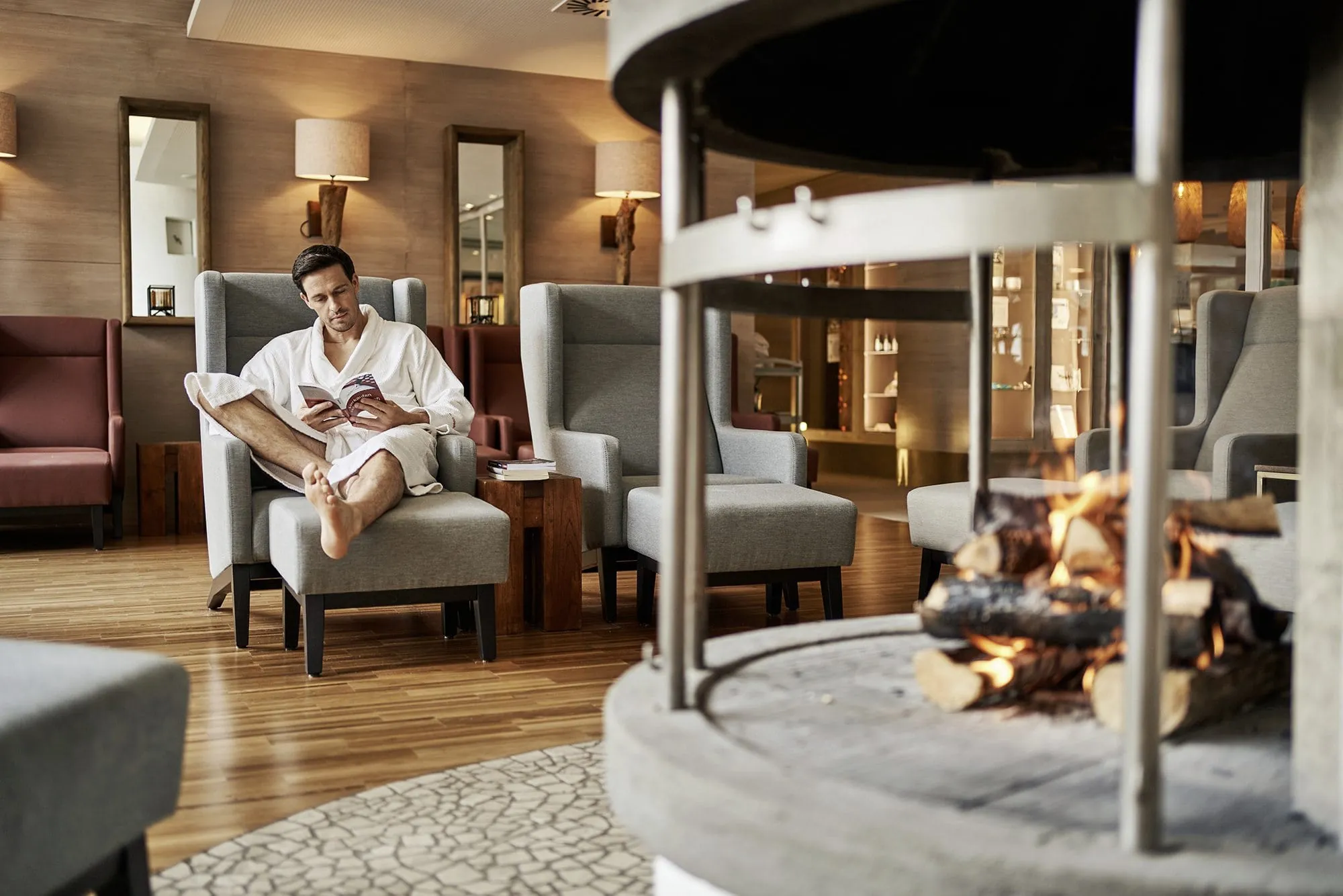 Mann im Bademantel liest am Kaminfeuer im Ruheraum des aja F&uuml;rstenhaus am Achensee