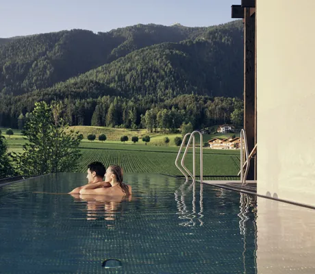 Paar schwimmt im Rooftoppool im Falkensteiner Kronplatz mit Blick auf den Kronplatz