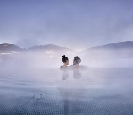 Paar steht am Beckenrand des Infinitypool im Falkensteiner Kronplatz im Winter
