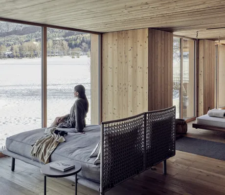 dunkelhaarige Frau sitzt auf der Doppelruhelieg im Ruheraum des Falkensteiner Kronplatz und schaut in die Ferne