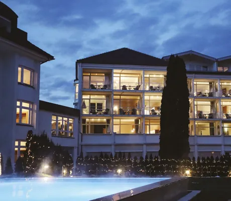 beleuchtete Fassade des Das Parkhotel mit geschmücktem Weihnachtsbaum und Blick über den Outdoorpool