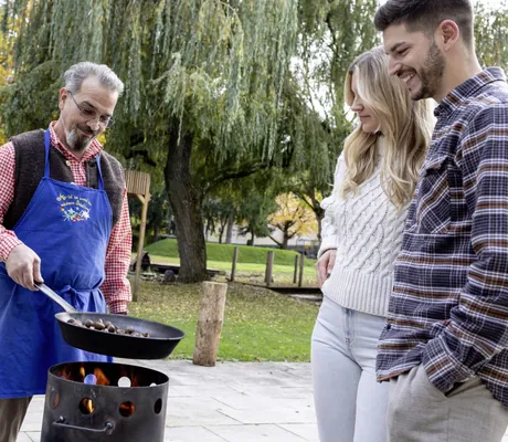 Mann in blauer Schürze röstet Kastanien in einer Pfanne über dem Feuer im Das Parkhotel