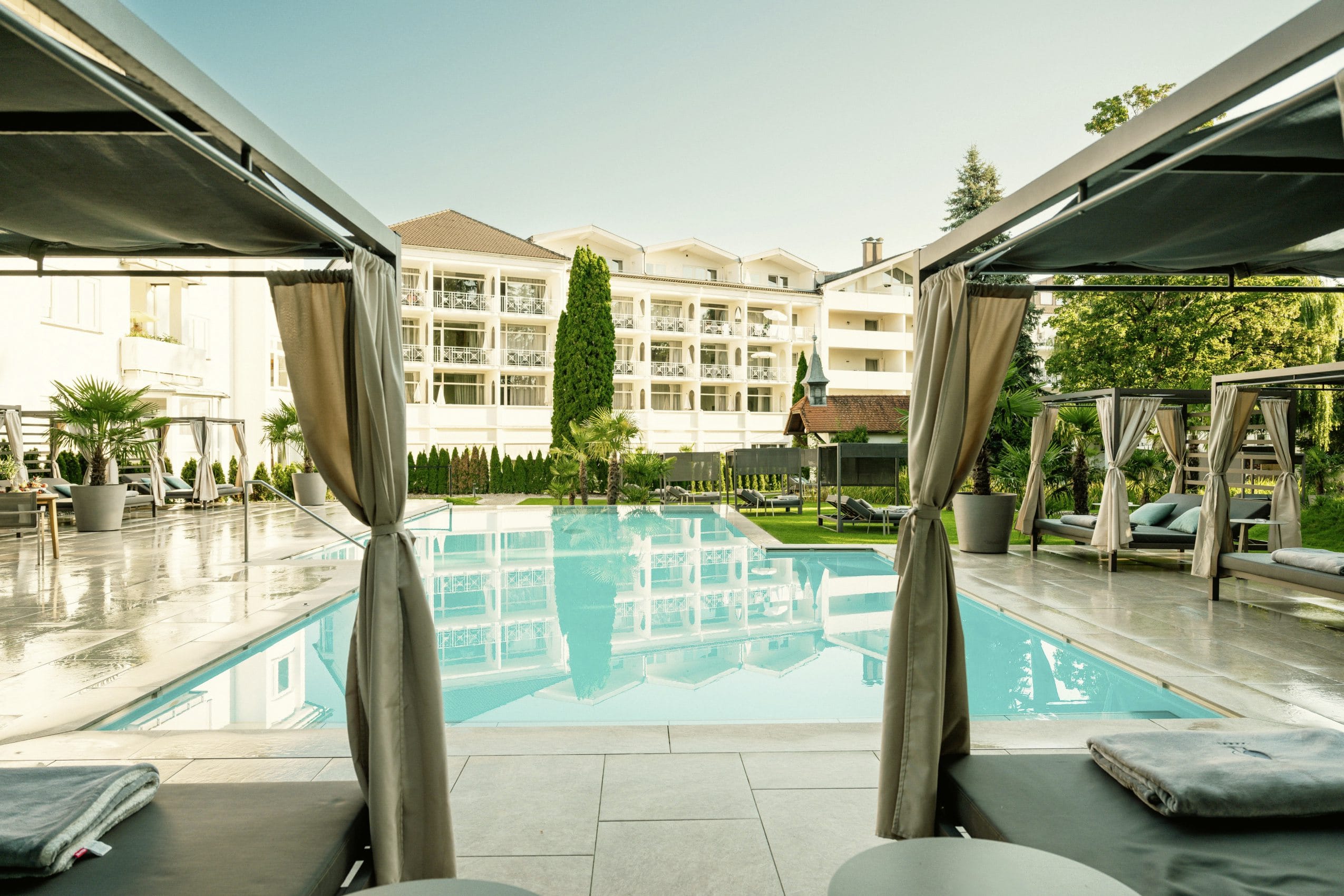 Blick von den Daybeds am Außenpool aus auf die Fassade des Das Parkhotel